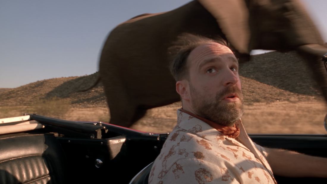 Driver in a convertible with an elephant passing behind